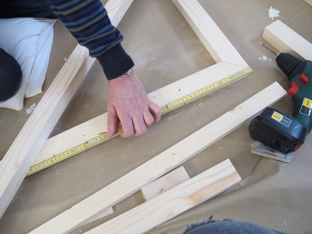 Nærbilde av hånd som måler blekt treverk med gult målebånd, pappunderlag og drill