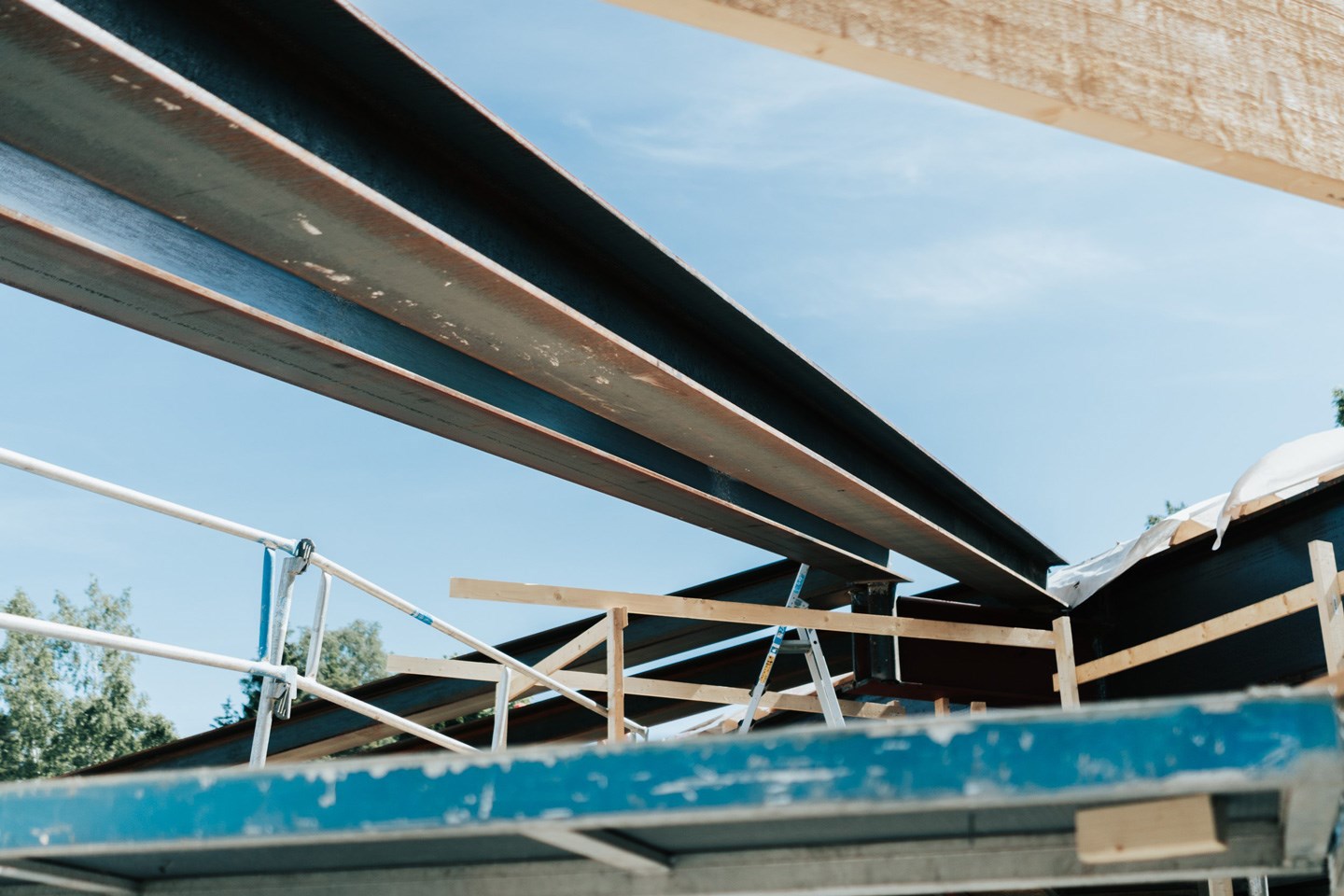 Takkonstruksjon under bygging med mørke stålbjelker, hvitt stillas og klar blå himmel.