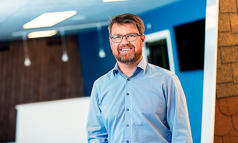 Mann i lyseblå skjorte står i moderne kontorlobby med blå og trefargede vegger.