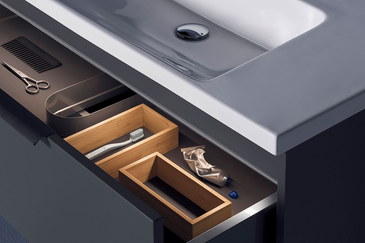 Åpen mørk skuff under hvit servant med treinndelere, tannbørste, klemt tannkrem, saks, kam