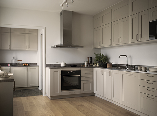 Lyst grått kjøkken med svart benkeplate, innebygd ovn, ventilator, treparkett og planter.