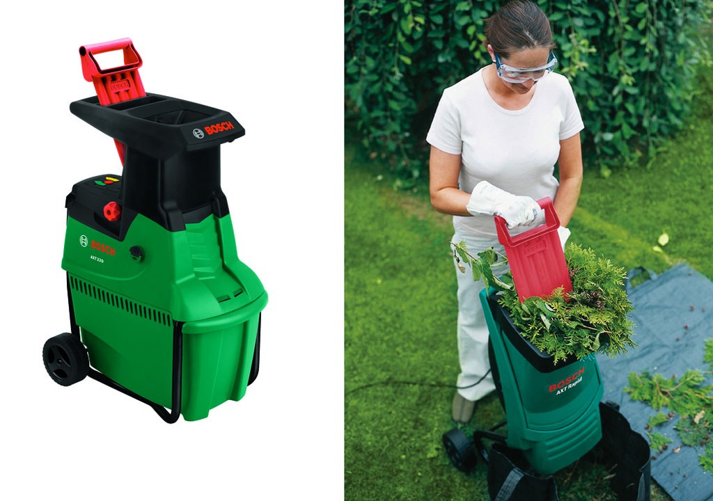 Grønn-svart Bosch hagekværn med rødt håndtak plassert på gressplen med grønne kvister