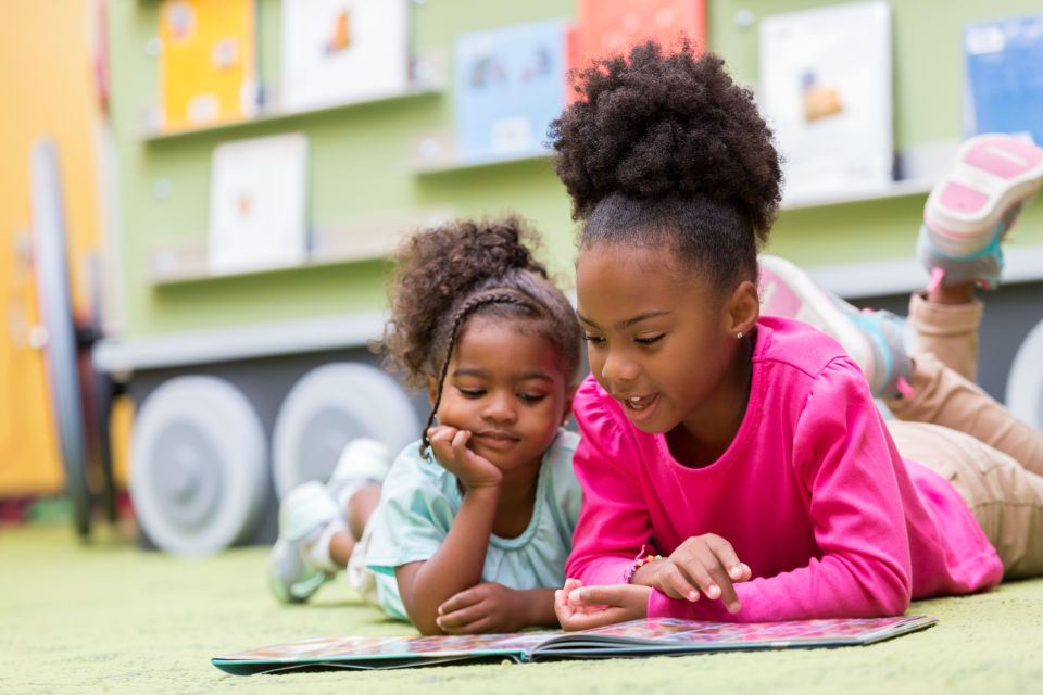 Two Girls laying on floor reading together in classroom