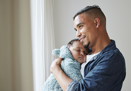 A new father holding his young child and smiling.