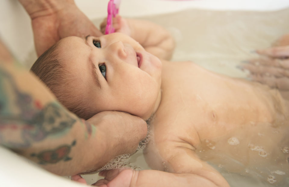 Infant in tub head being held by parent