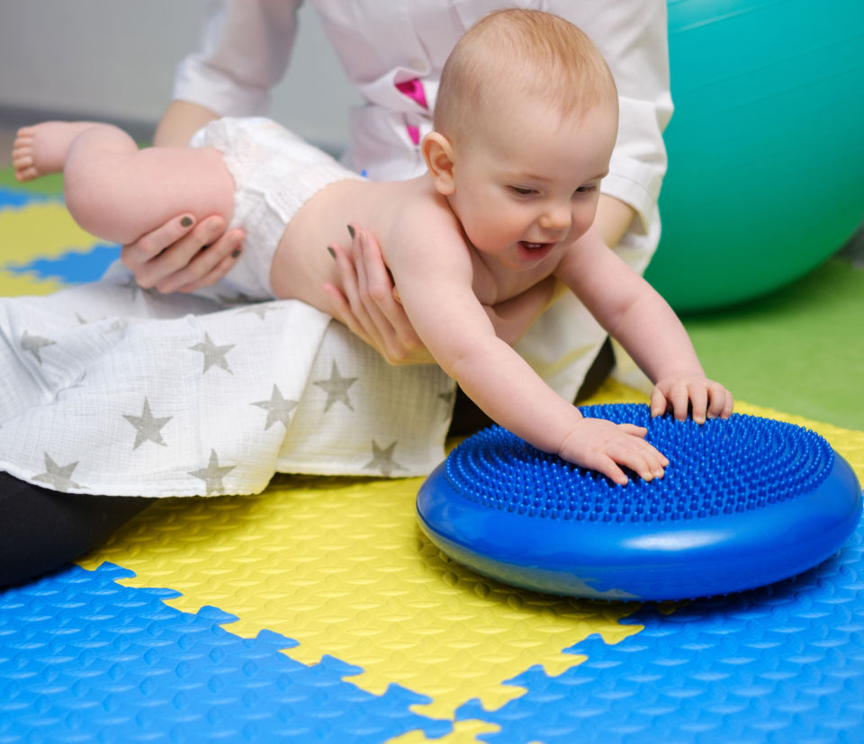 Baby lightly being picked up to play with blue toy