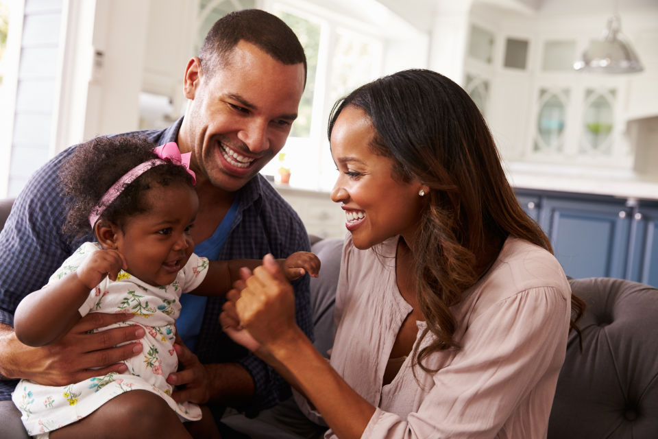 Parents sitting on couch daughter in dads lap mom squeezing daughters hand in excitement