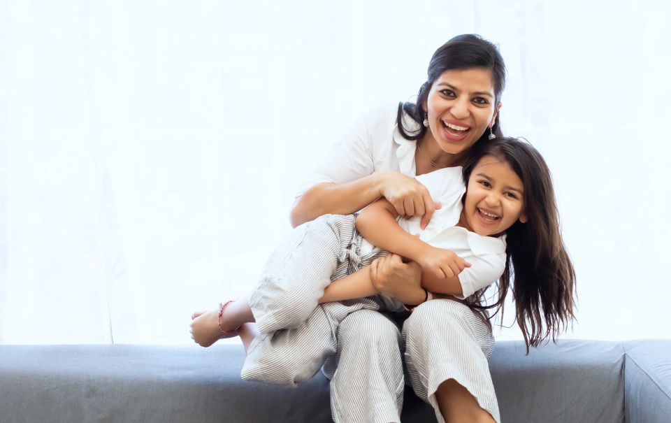 Mother and daughter laughing and hugging on couch