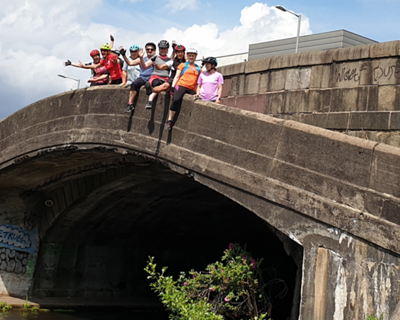 Group of people in helmets sat on a bridge after cycling