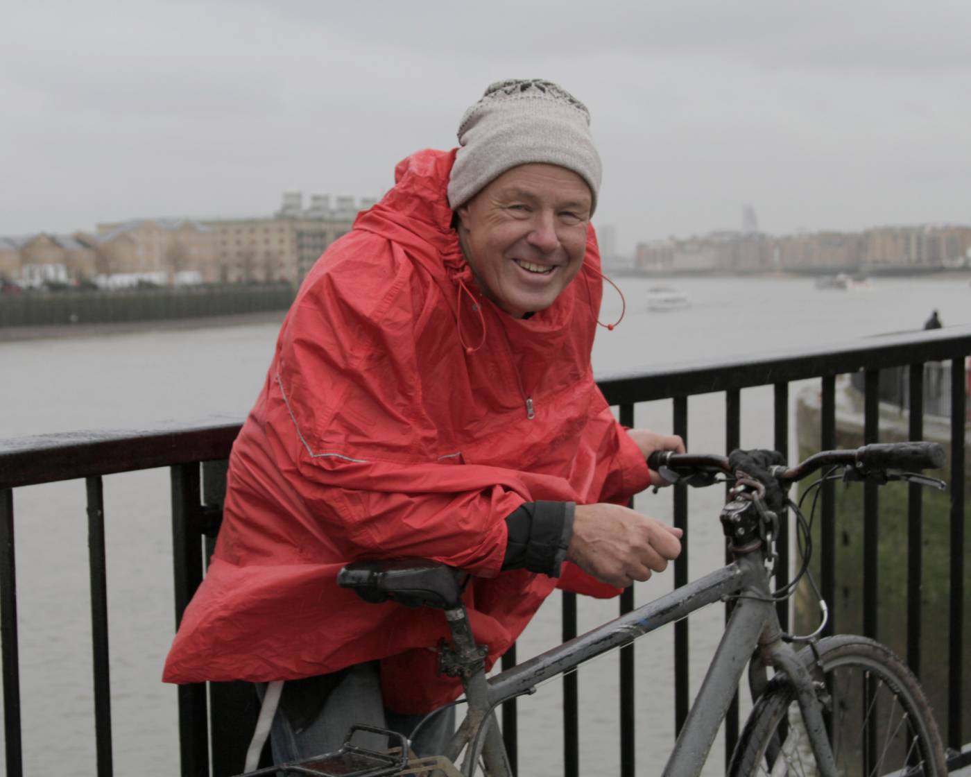 Man wearing a raincoat standing in the rain by his bike
