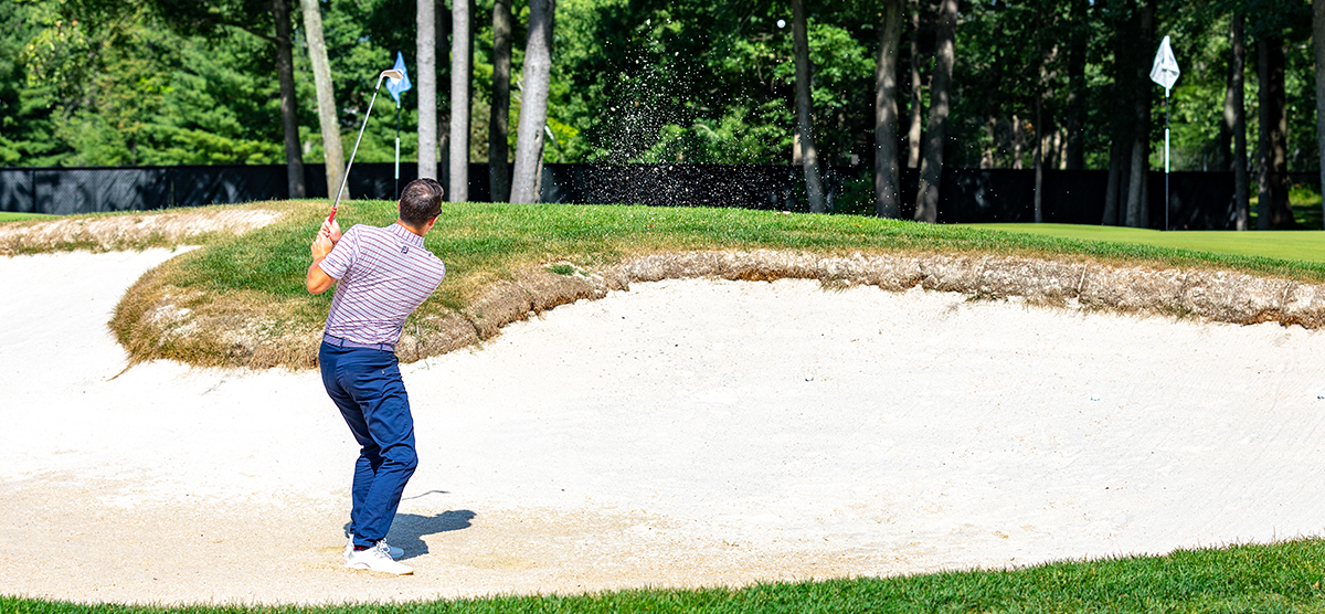 Player hitting out of the greenside bunker next to the practice putting green at SentryWorld