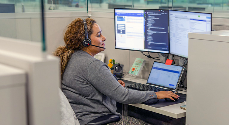 Woman talking with a customer through a headset while working on a computer.