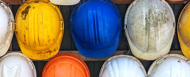 Blue, yellow, white, and orange hard helmets hung up on a wall