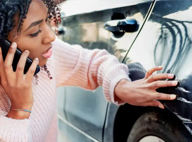 a woman on her cell phone while inspecting car damage