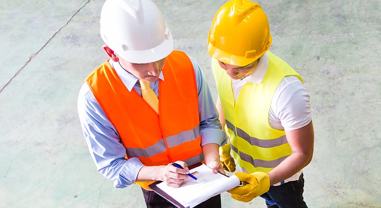 Two men in hard hats near forklift looking at clipboard