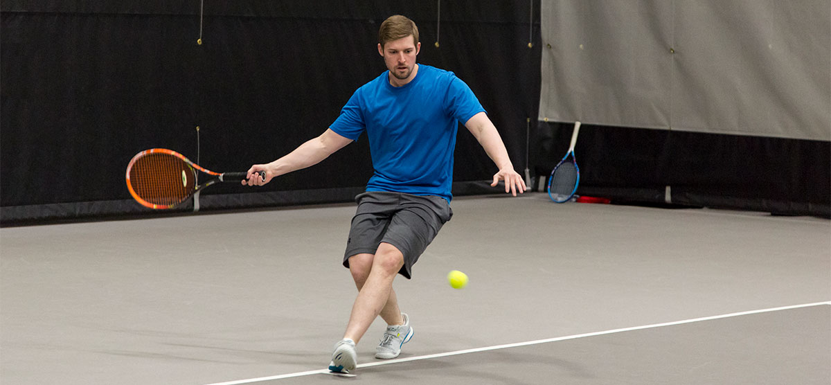 Player hitting a tennis ball on a court in the SentryWorld fieldhouse