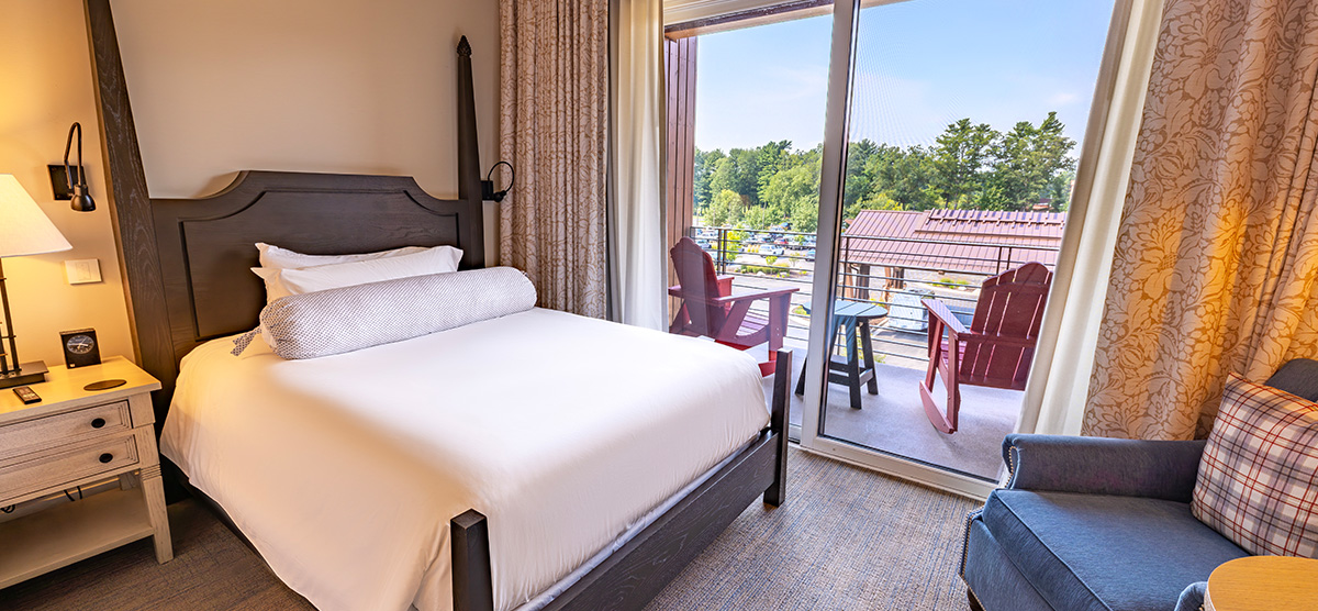 carousel-executive-queen-terrace-2-1200x556 Bed next to a patio door overlooking the hotel front entrance.