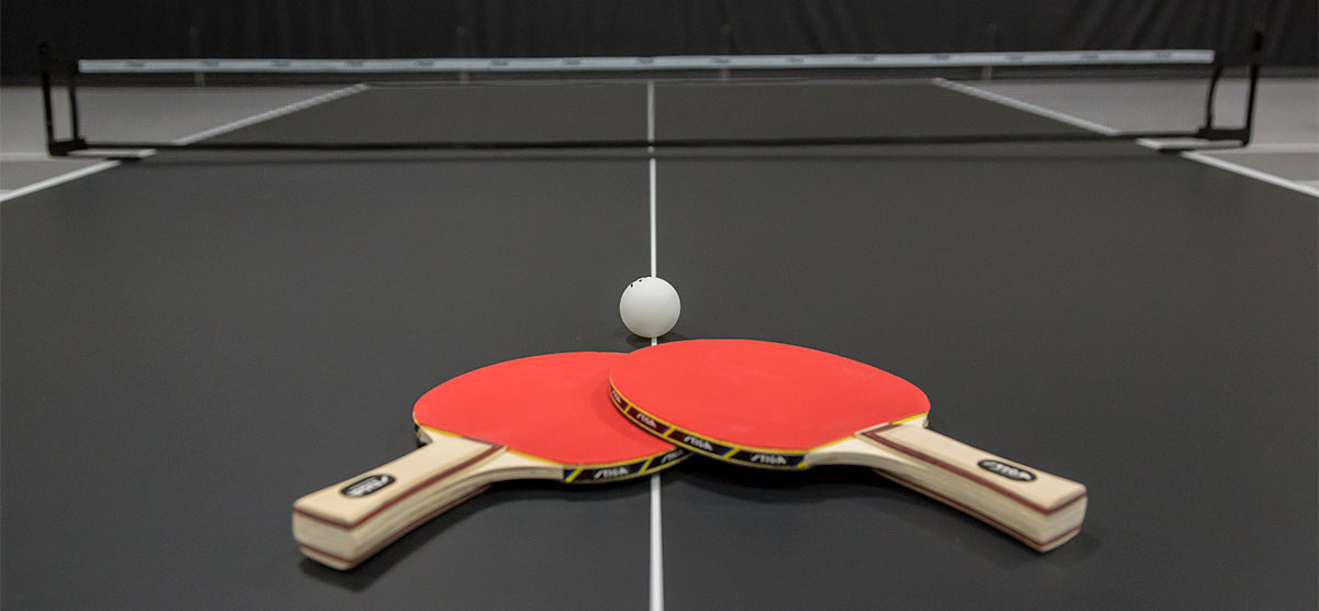 Two table tennis paddles and a ball on a table in the fieldhouse