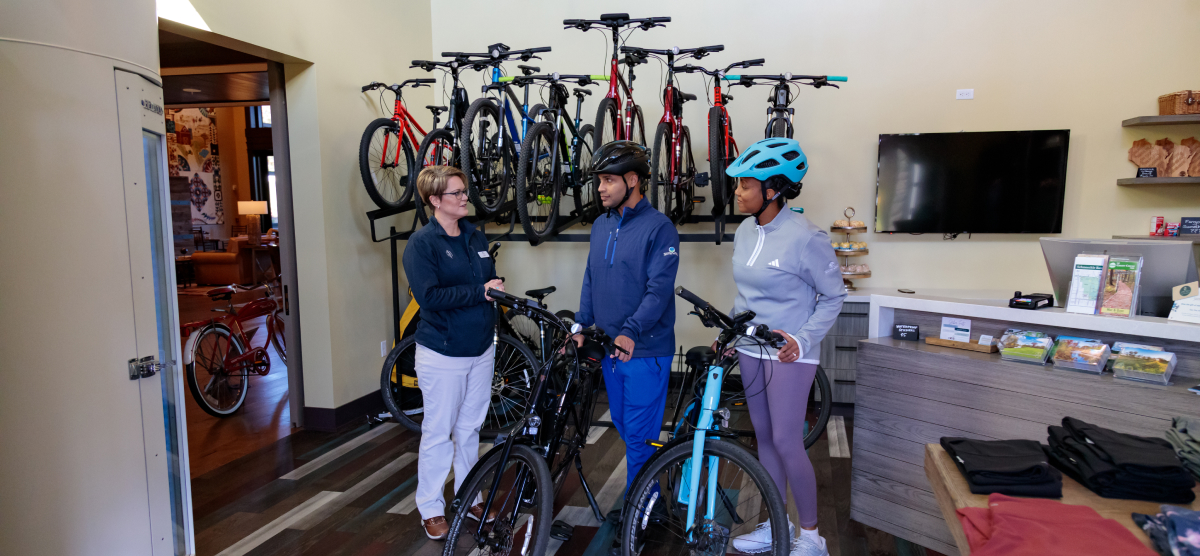 An employee assists two customers with bicycles in a bike rental shop or store.