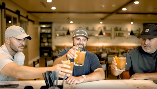 Three men holding cocktails while sitting at the Library cafe bar.