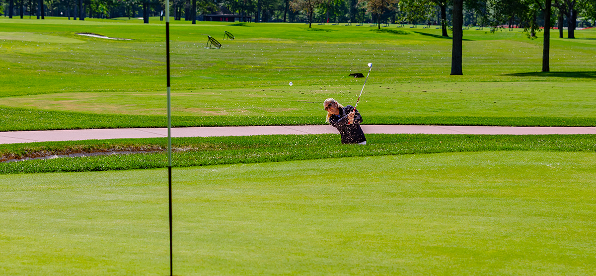 Player hitting out of a sand trap next to the practice putting green at SentryWorld