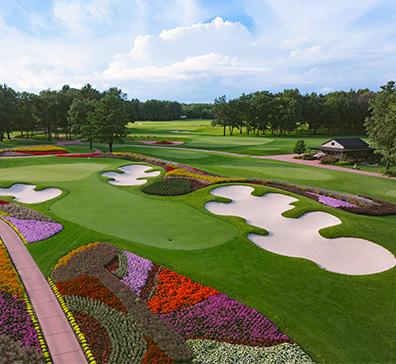 image-card-contact-sentryworld-396x364 Aerial view of the SentryWorld golf course with colorful flower beds, sand traps, and green fairways.