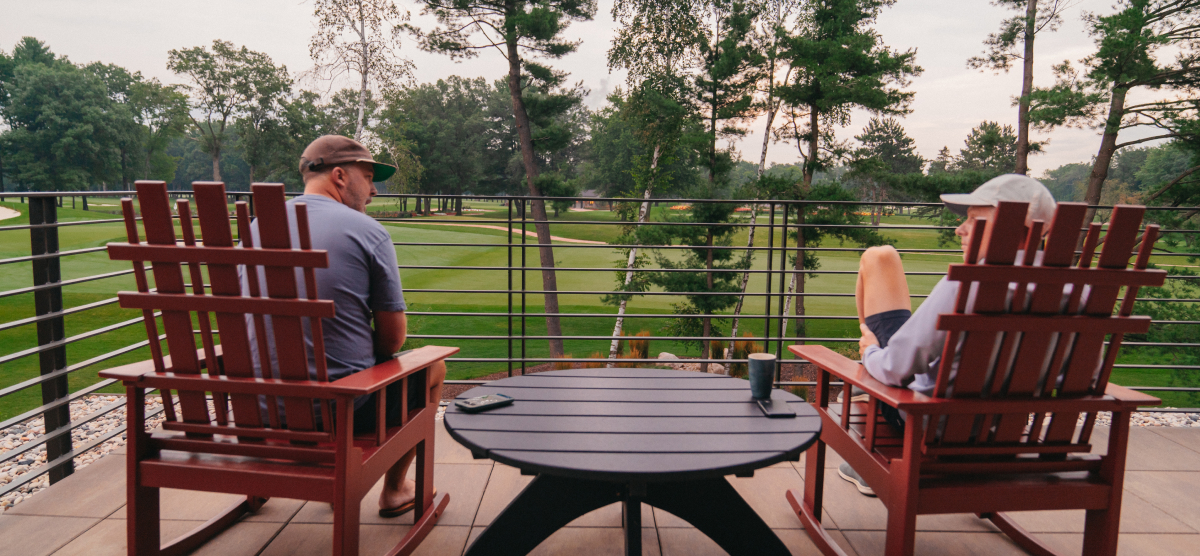 Two people sitting in adirondack chairs on a deck overlooking the 18th hole at SentryWorld.