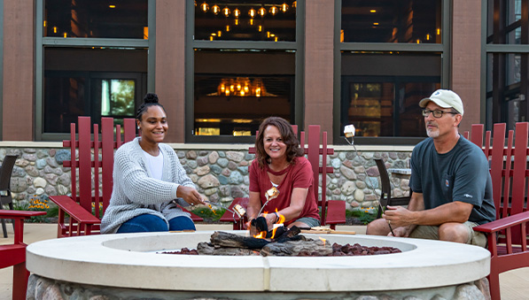 50-50-lodging-amenities-explore-resort-597x339 Three people roasting marshmallows around an outdoor fireplace at The Inn.