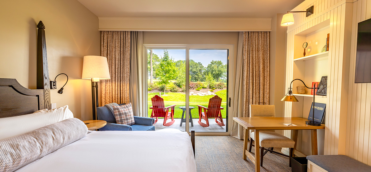carousel-golf-view-king-terrace-2-1200x556 King bed with a chair, desk, and patio door overlooking the golf course.