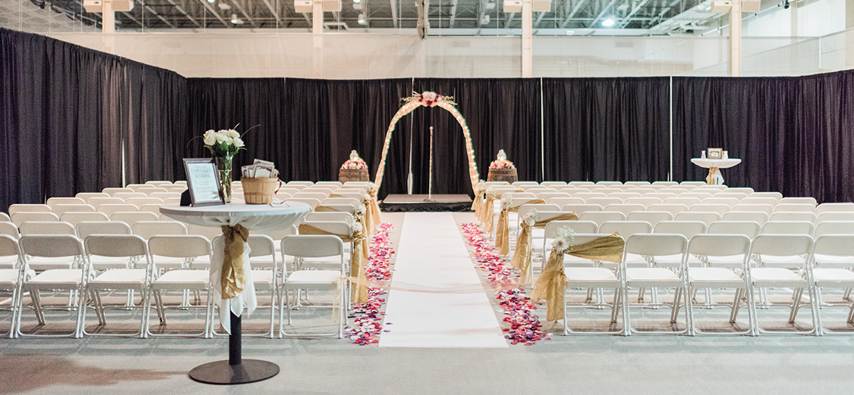 carousel-wedding-venue-fieldhouse-2-1200x556 Rows of white chairs set up for a wedding ceremony in the fieldhouse.