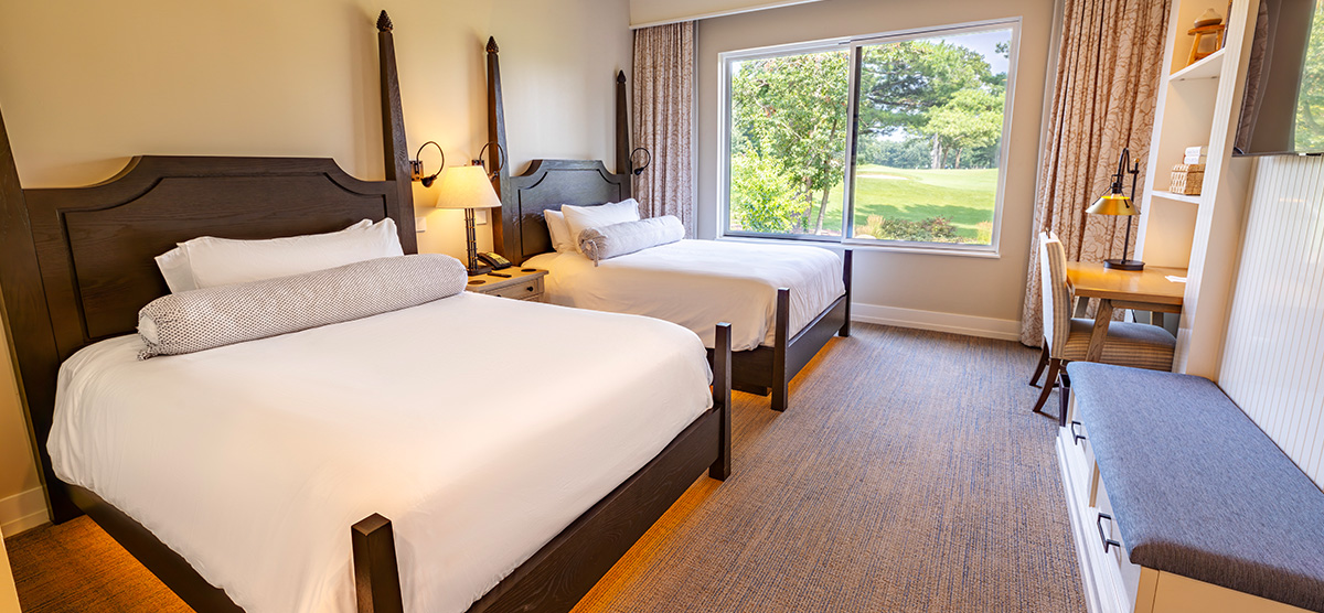 carousel-suite-golf-view-queen-1-1200x556 Two queen beds with desk area and bench.