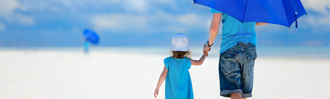 Child and parent walking on beach under umbrella