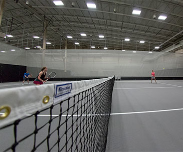 Tennis court net and players on a court in the SentryWorld fieldhouse