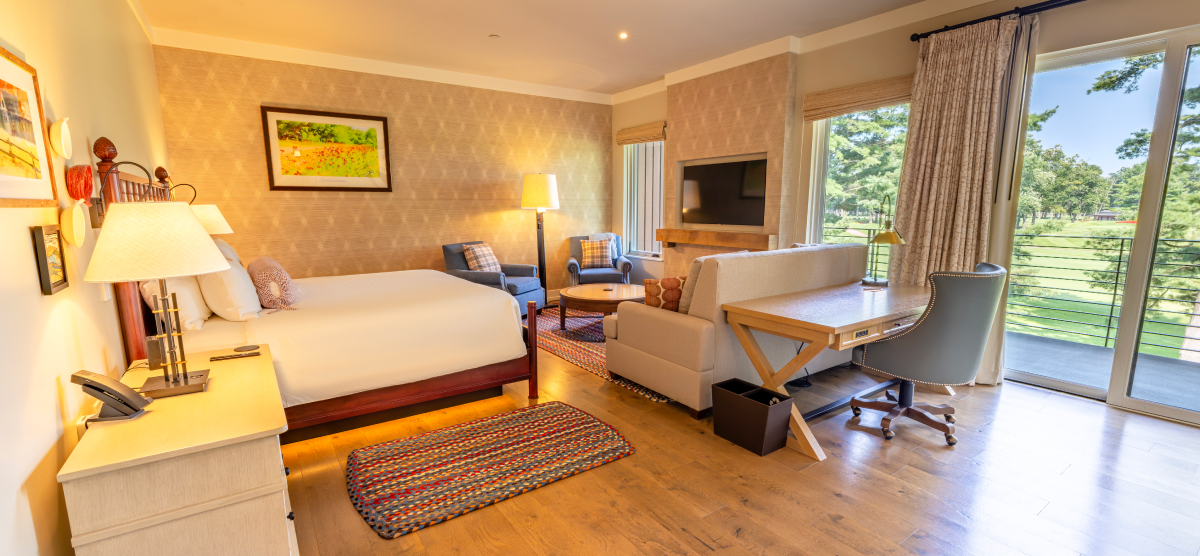 Hotel room with a king size bed, seating area, and balcony overlooking hole 18. 