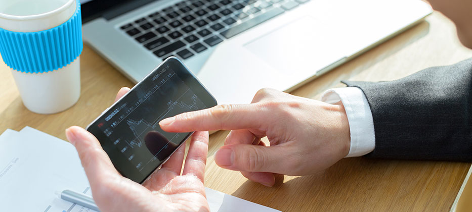 Business man at desk checking graph on phone