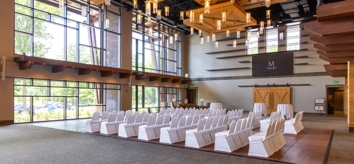 Indoor event space with rows of white chairs and large windows.