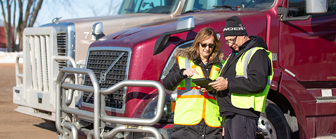 Two drivers looking at tablet near trailer trucks