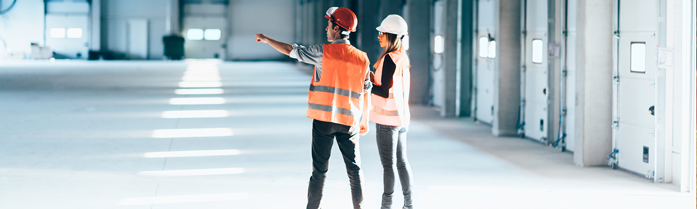 Two people in safety gear planning in warehouse