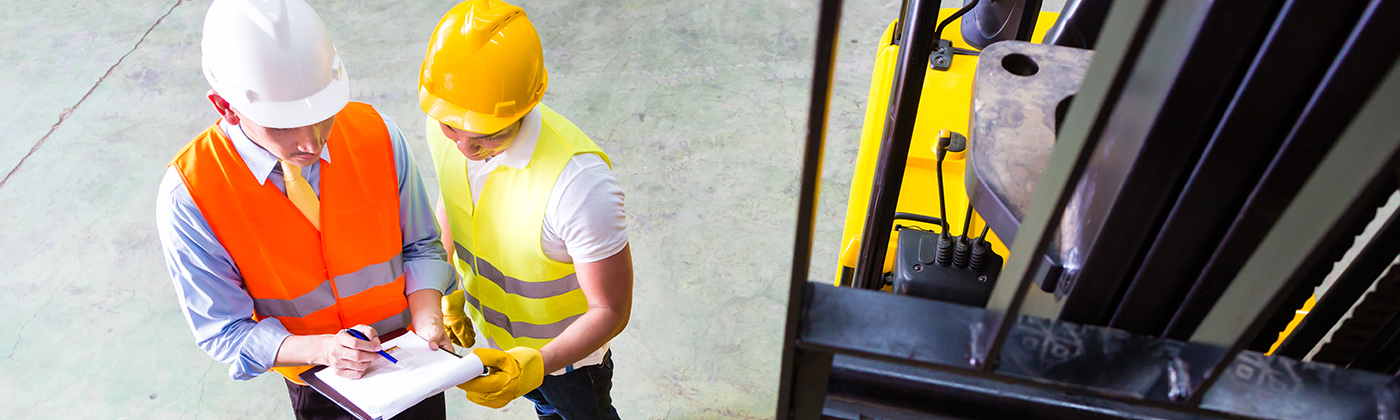 Two men in hard hats near forklift looking at clipboard