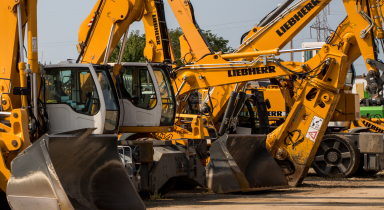 Row of yellow construction vehicles, including excavators and wheel loaders, parked outdoors.