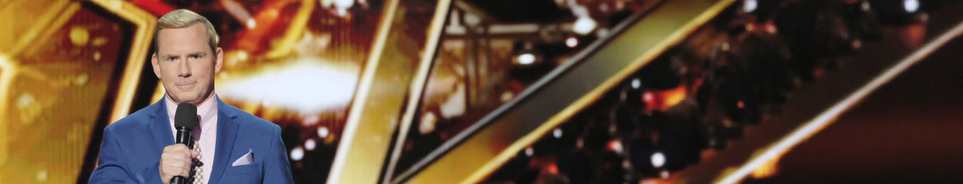 Tom Cotter, a white male, holding a microphone with a gold star background. 