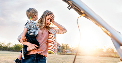 Frustrated mom holding her baby and standing by broken down car