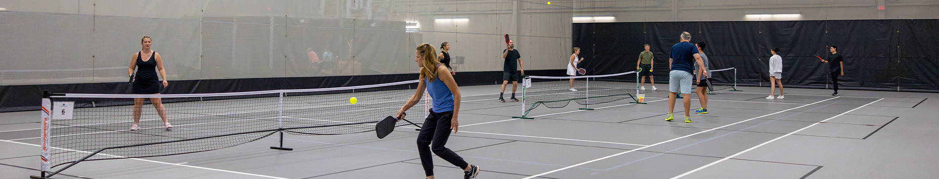 Multiple people playing pickleball on an indoor court. 
