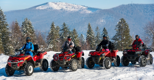 Group of people on off road vehicles in the winter with a mountain in the background.