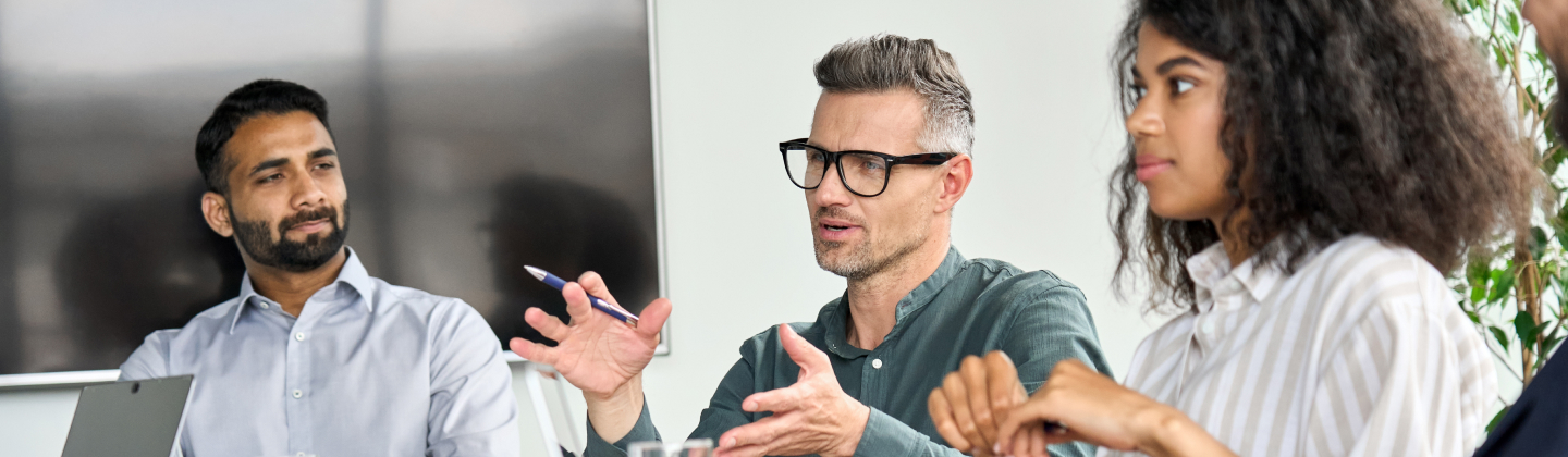 Group of professionals in a meeting, with one man speaking and gesturing.