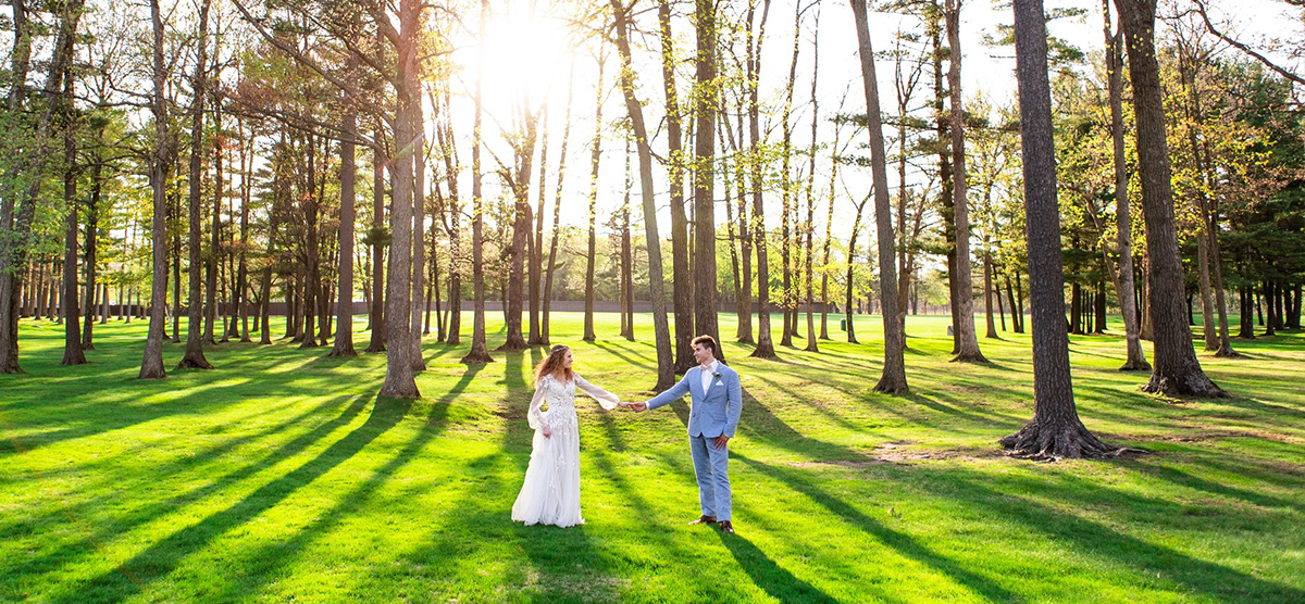 Bride and groom holding hands in a wooded area at SentryWorld