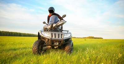 Person wearing a helmet and riding an ATV in an open grass area. 