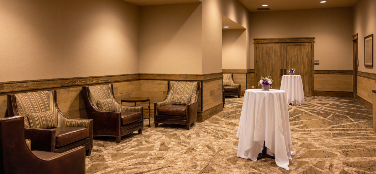 Lounge area with armchairs, two high-top tables with flowers, and patterned carpet.