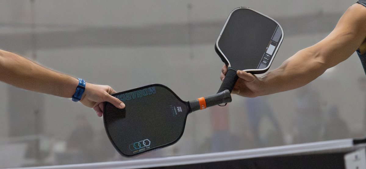 Two people clinking pickleball paddles together over a net.