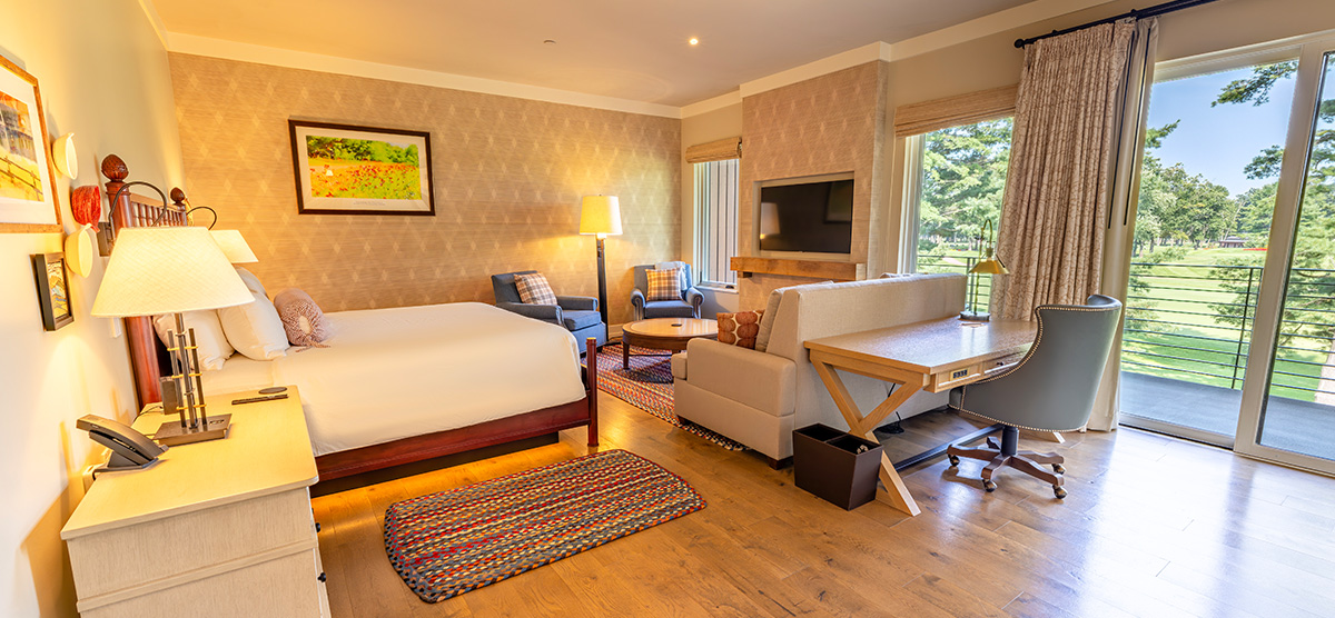 carousel-executive-junior-suite-1-1200x556 King bed with seating area, desk, and patio door overlooking the golf course.